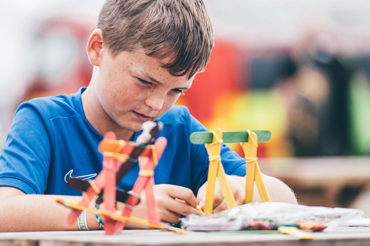 Child in a blue shirt assembling colourful popsicle stick structures at a table