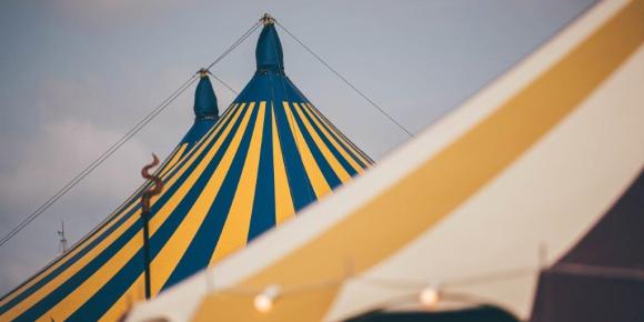Yellow and blue stripy pavilion behind a yellow and white stripy tent against a cloudy sky