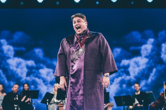 Nathan James Dearden,winner of the 2024 Medal y Cyfansoddwr during the ceremony on the Pavilion stage wearing a purple cloak with a blue background