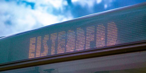 A digital display on a bus showing the destination 'EISTEDDFOD' against a background of a partly cloudy sky