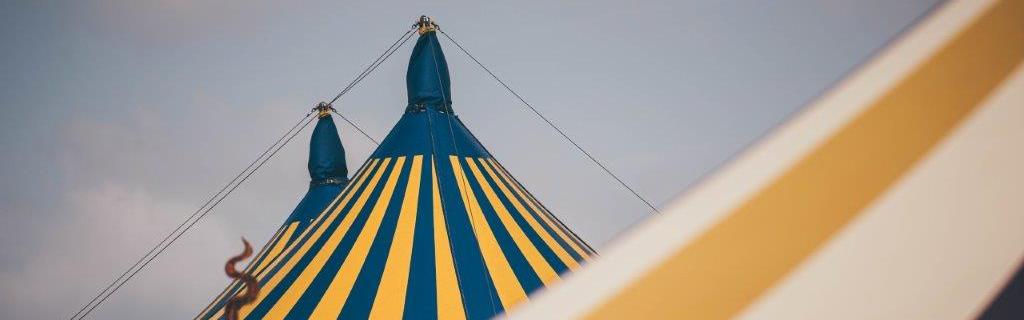 Yellow and blue stripy pavilion behind a yellow and white stripy tent against a cloudy sky