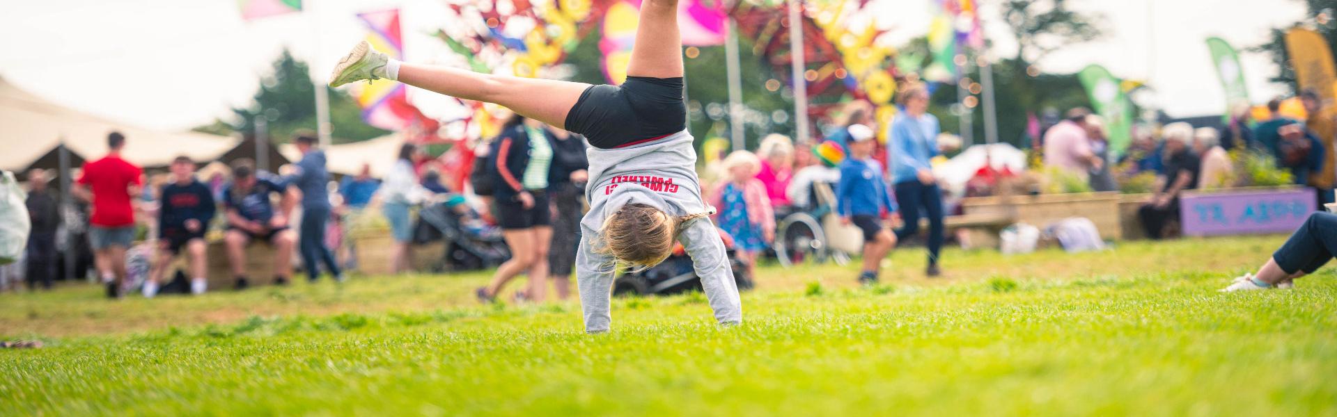 Girl performing a cartwheel in front of the Pentref Plant sign