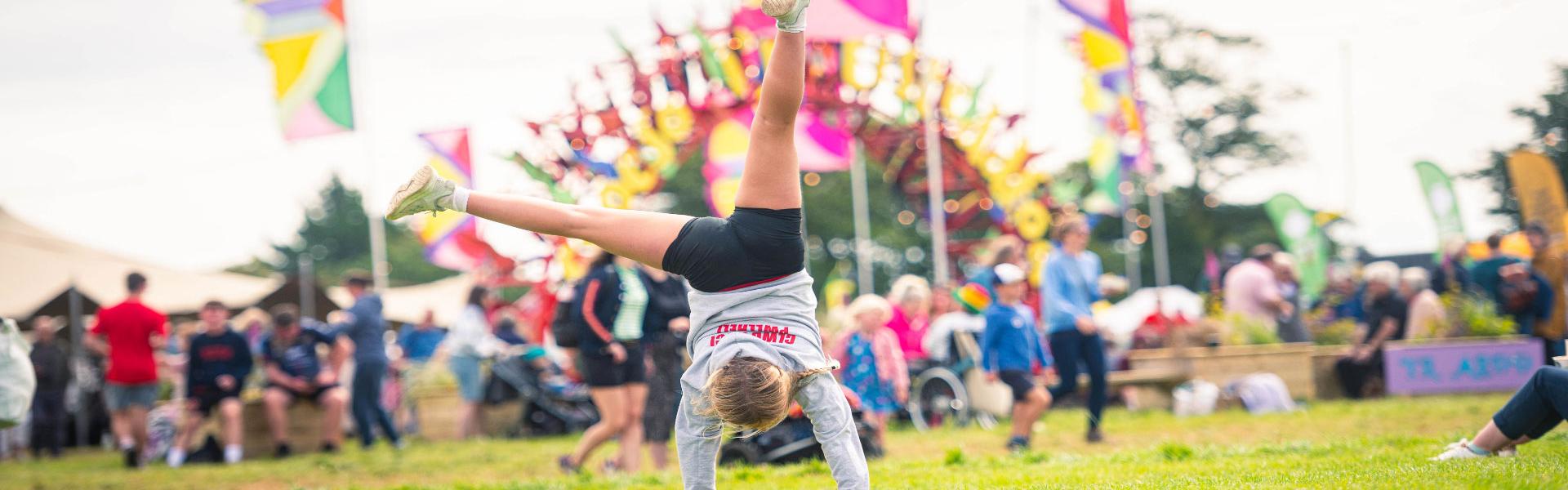 Girl performing a cartwheel in front of the Pentref Plant sign