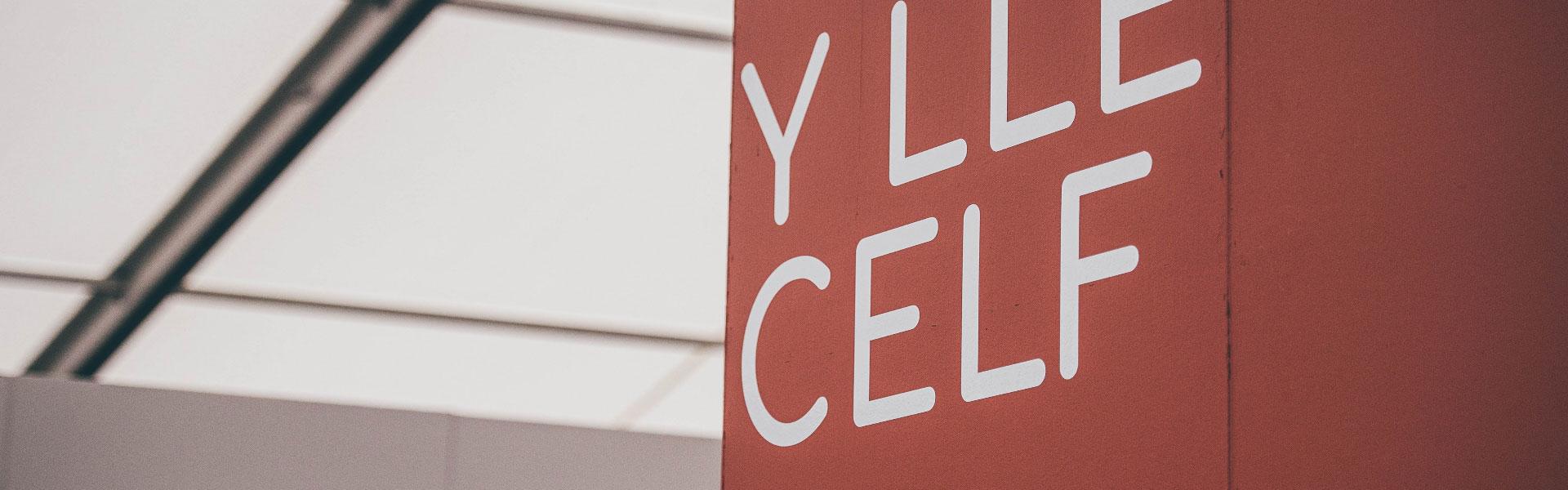 Red sign in temporary building with the words The Art Place (Y Lle Celf) in white capitals