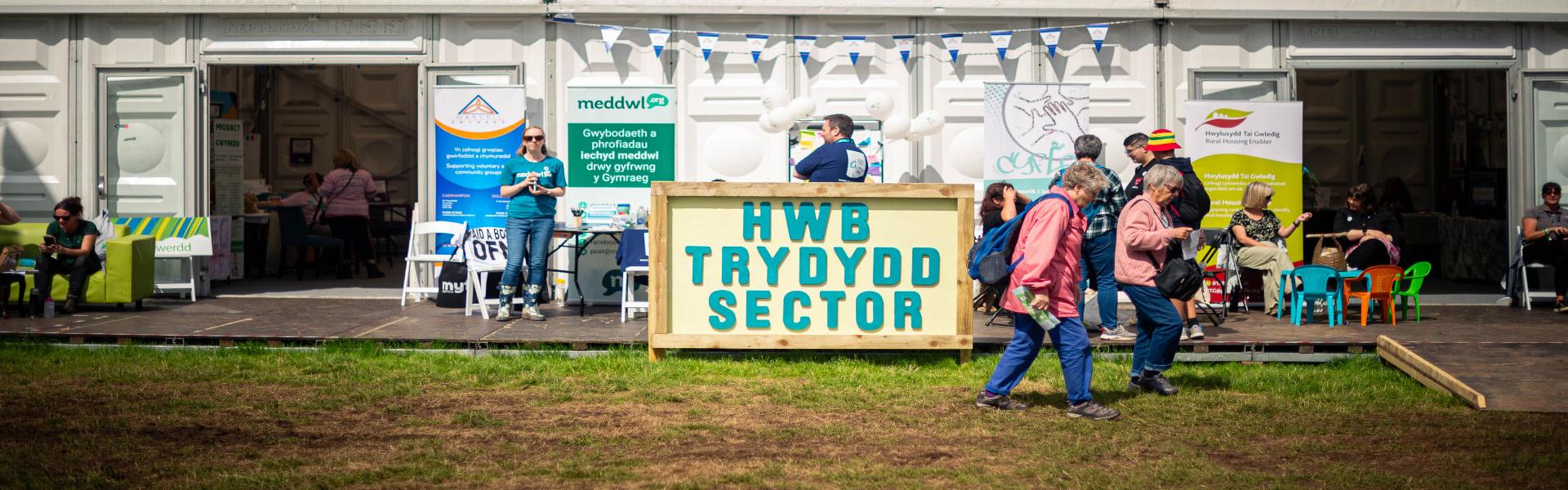 A wooden sign with a yellow background and the words Third Sector Hub in Welsh on it 