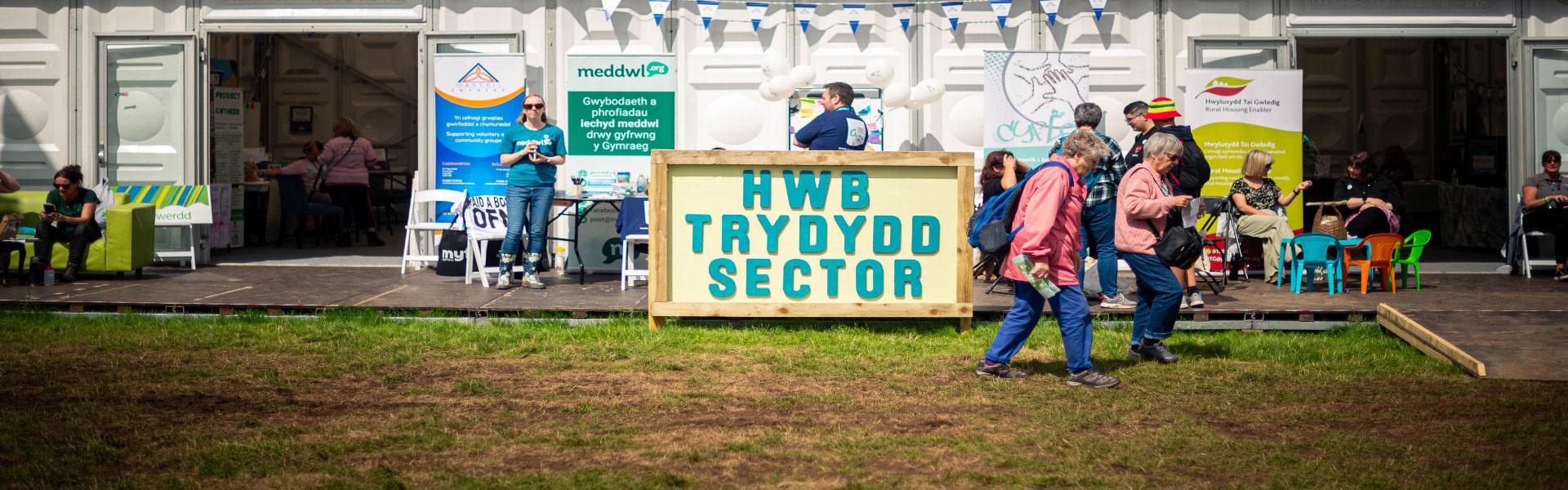 A wooden sign with a yellow background and the words Third Sector Hub in Welsh on it 