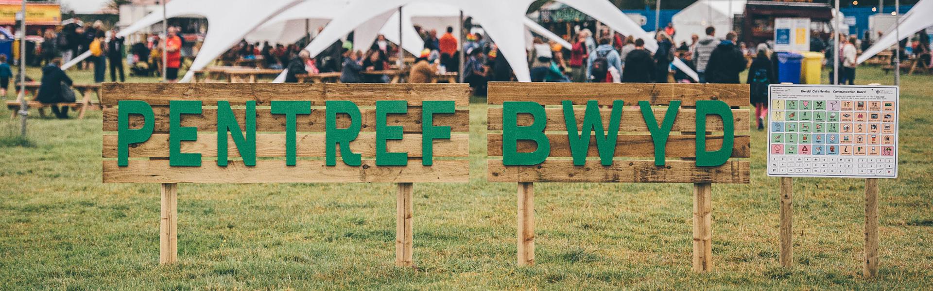 Food Village sign in front of a white tent on the Maes under a grey sky