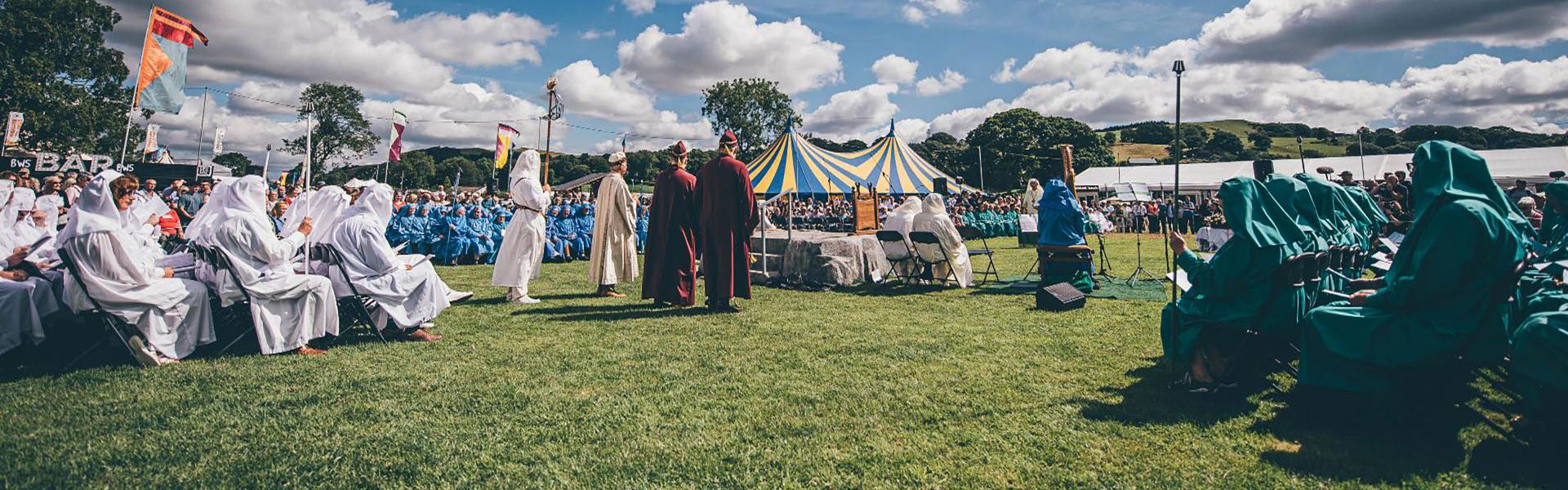 The Gorsedd Circle under a blue sky with a few clouds.  There is a blue and yellow striped pavilion in the background