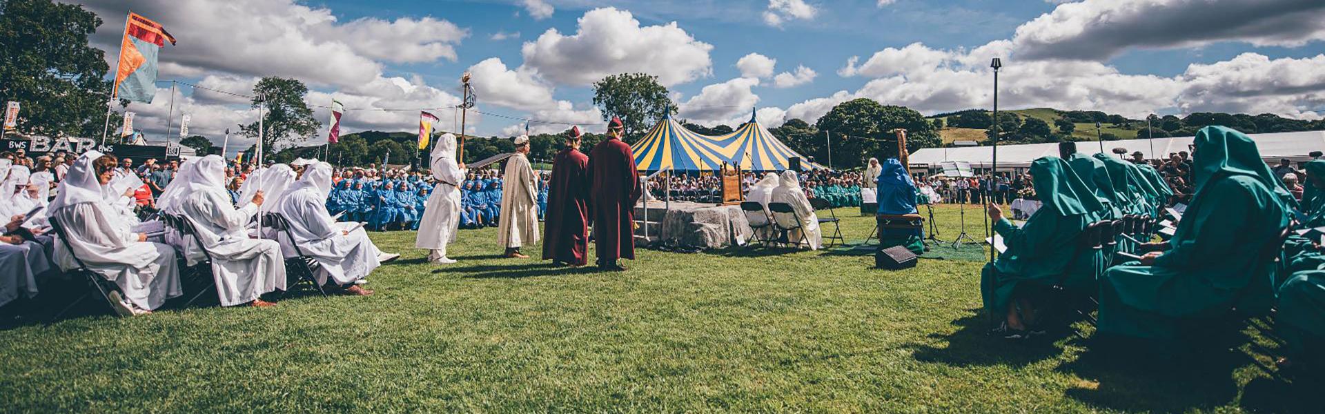 The Gorsedd Circle under a blue sky with a few clouds.  There is a blue and yellow striped pavilion in the background